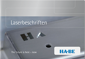 Eine metallische Oberfläche wird durch einen Laserstrahl mit den Buchstaben HA graviert. Oben steht der Text Laserbeschriften und unten The future is here - now. In der rechten unteren Ecke befindet sich das HA-BE-Logo.