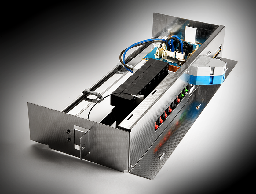 Ein metallisches Elektronik-Rack mit freiliegenden internen Komponenten, einschließlich Leiterplatten, Verkabelung, einem schwarzen Relaisblock, farbigen Schaltern und einem angeschlossenen blauen Ethernet-Kabel. Die Seitenwand ist offen und gibt den Blick auf die Schaltkreise im Inneren frei.