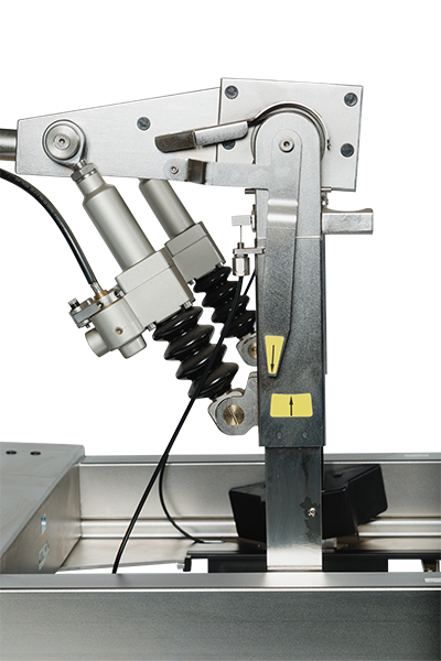 Nahaufnahme einer industriellen Maschinenkomponente aus Metall mit Hydraulikzylindern, einem aufgewickelten schwarzen Kabel und gelben Warnhinweisen vor einem neutralen Hintergrund.