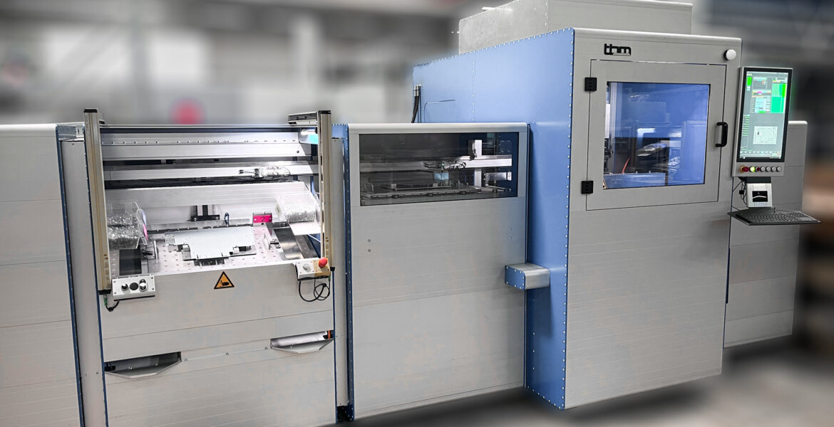 Eine große Industriemaschine mit Schalttafel und Bildschirm, Metallfächern und Schutzglastüren in einer modernen Fabrikumgebung.